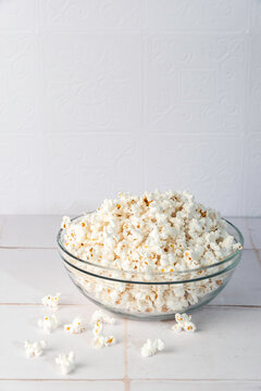 Popcorn in a clear glass bowl on a white tile surface 
