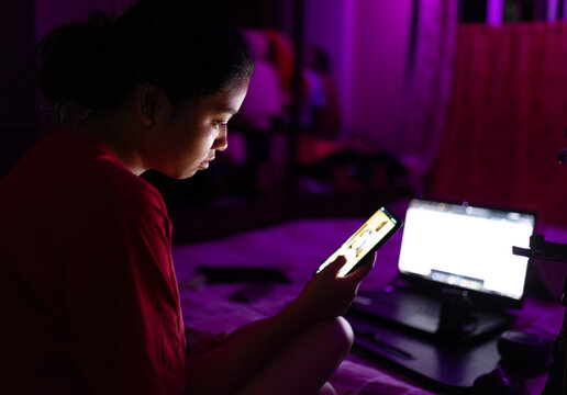 Indian young woman browsing internet in smartphone at night inside 