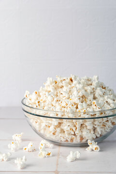 Popcorn in a clear glass bowl on a white tile surface 