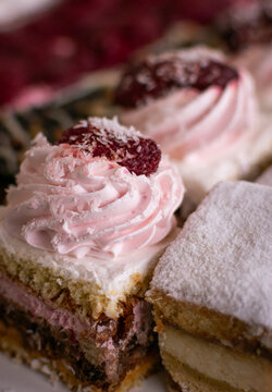 Detalle macro de un mini pastel en capas con crema rosa, frambuesa y coco, junto a un bocado espolvoreado con az&uacute;car. Reposter&iacute;a fina para eventos.