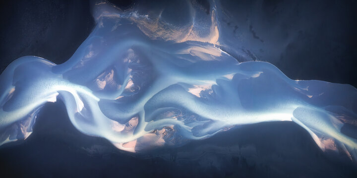 Aerial view of a braided glacial river with intricate blue channels and dark sediment patterns flowing through the Southern Region, Iceland.