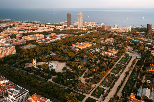 Aerial view of Parc de la Ciutadella with lush greenery, central lake, and historic buildings, set against the urban skyline and Mediterranean Sea in Barcelona, Catalonia, Spain.