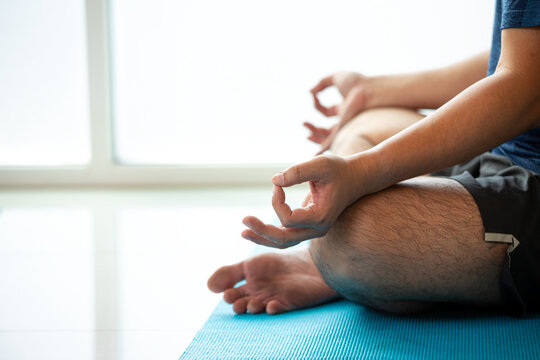 Man practicing meditation and yoga with mudra in lotus pose on a blue mat, showing mindfulness, wellness, balance, relaxation, breathing, focus, calm, and indoor fitness