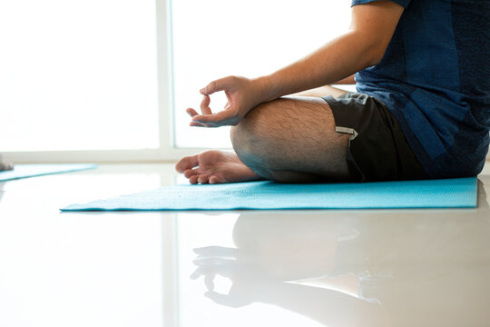 Man practicing yoga meditation in lotus pose on a blue mat with mudra, mindfulness, wellness, balance, relaxation, breathing, focus, calm, fitness, and bright indoor copy space