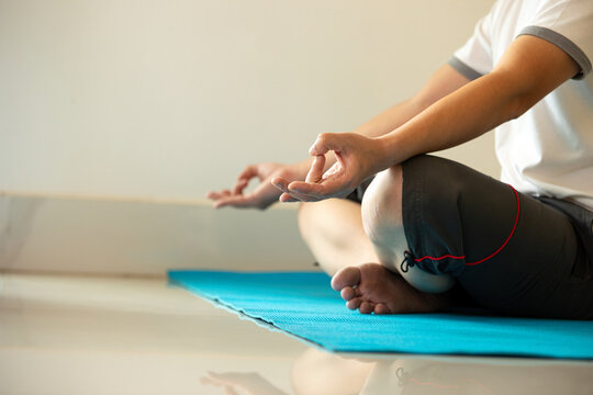 Man practicing yoga meditation in lotus pose on a blue mat with mudra, showing mindfulness, wellness, balance, relaxation, breathing, focus, calm, fitness, and indoor tranquility