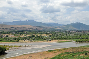 Landscape view of the Mtkvari (Kura) River flowing through a green valley with mountains near Uplistsikhe, Georgia © MikhailT