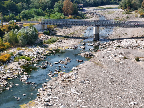 Aerial view of the Sesia River with low water levels and exposed rocky riverbed beneath a metal bridge in Vercelli, Piemonte, Italy.
