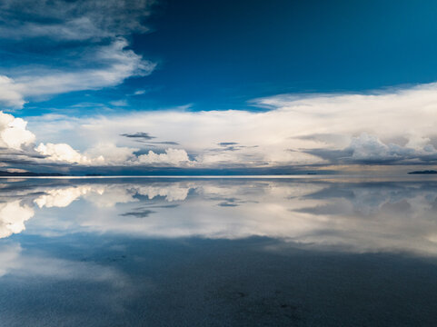 Aerial view of the Uyuni Salt Flat with a perfect mirror reflection of the dramatic clouds and blue sky on the water-covered surface in Potosi Department, Bolivia.
