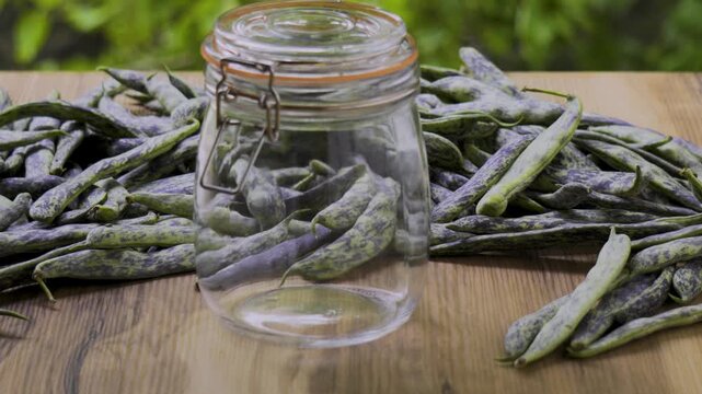 Green beans with closed jar on wooden table with leaves background, 4K