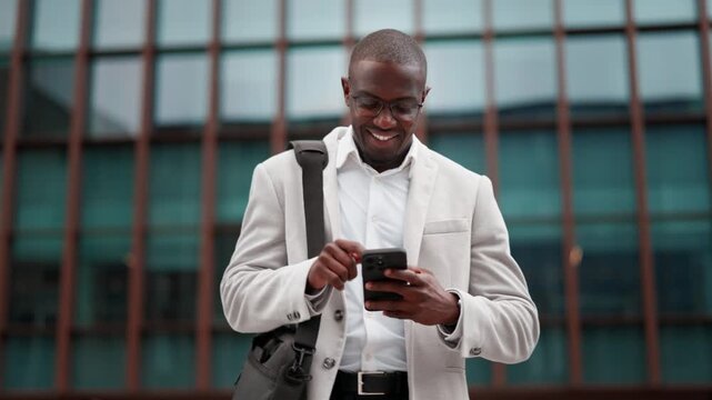 Black businessman, using smartphone, texting, outdoor near office building. African american business man smiling, works as business owner, focused on daily tasks, building strong client partnerships.