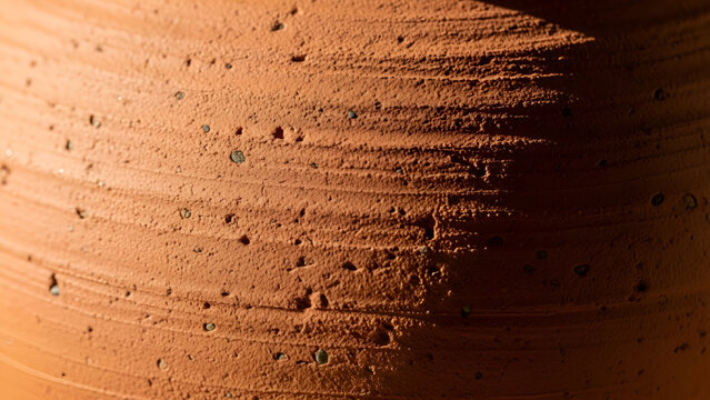 Rough terracotta clay surface displays detailed horizontal ridges and porous natural textures under harsh dramatic lighting