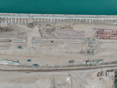 Aerial view of Kali Baru port area showing construction equipment, piles of sand, and industrial infrastructure along the waterfront in Cilincing, Jakarta, Indonesia.