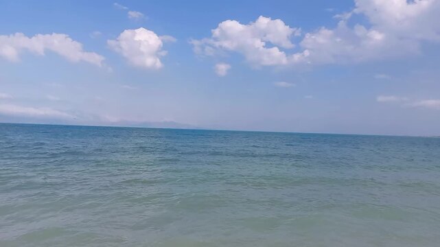Beautiful calm blue water of Lake Sevan with fluffy white clouds in Armenia. Peaceful wide view of calm blue water surface and gentle ripples on Lake Sevan under bright sunny sky with fluffy white clo