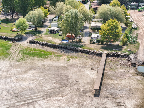 Aerial view of the dried shoreline of Lake Maggiore in Monvalle, showing exposed mud and low water levels due to drought, with a nearby campsite in Monvalle, Lombardy, Italy.