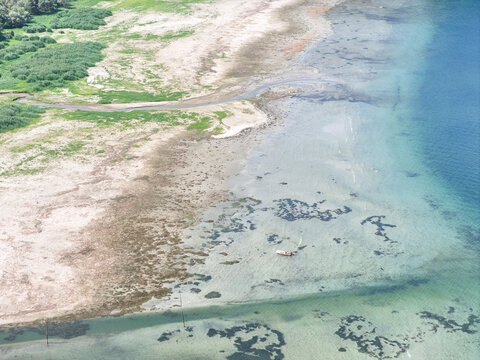Aerial view of the receding shoreline of Lake Maggiore showing exposed lakebed and a small boat stranded in shallow water due to record low water levels in Monvalle, Lombardy, Italy.