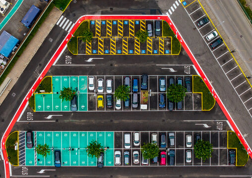 Aerial view of Designer Outlet Serravalle parking lot with marked accessible spaces, trees, and parked cars in Serravalle Scrivia, Piemonte, Italy.
