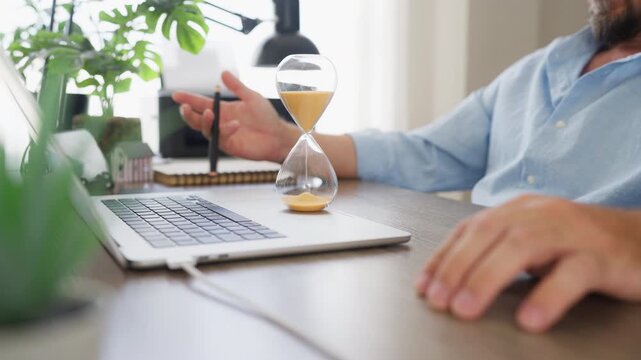 Professional businessman sitting at a desk with a laptop, hourglass and pen while organizing daily work. Productivity, focus, business workflow and office efficiency concept.