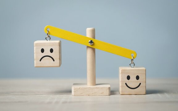 Wooden balance scale with sad and happy face blocks on a table