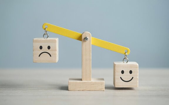 Wooden balance scale with sad and happy face blocks on gray background