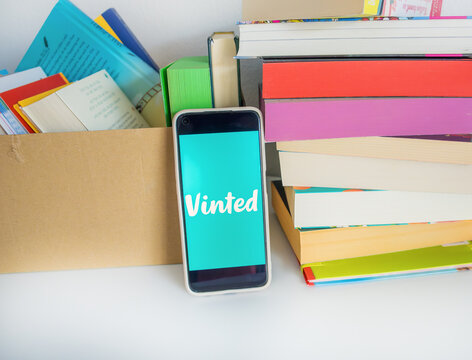 Braunschweig, Germany - August 06, 2026: Smartphone displaying Vinted logo app on screen placed between cardboard box and stack of colorful books, sustainable recommerce, decluttering, resale.