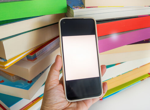 Mobile phone blank white display template in hand with multi-colored textbooks background, concept - online library app, digital book reading, educational presentation, contemporary academic research.