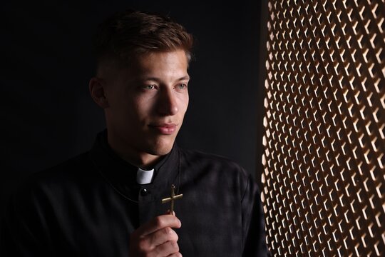 Priest with cross near partition in confessional booth