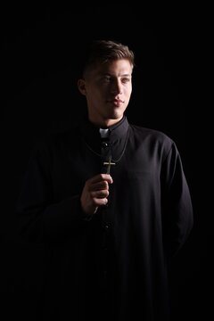 Priest in cassock with cross on black background