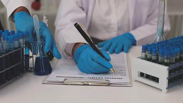 Biomedical researchers examining viral cultures while documenting experimental results on computer in sophisticated laboratory.
