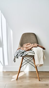 A clean minimal room with a single wooden chair and clothes casually placed over its back in soft natural daylight with neutral walls and a quiet uncluttered composition