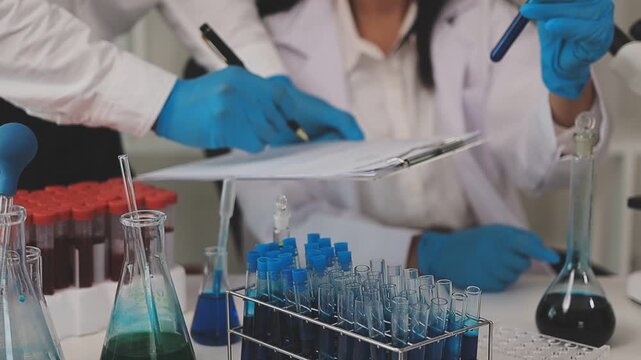 Biomedical researchers examining viral cultures while documenting experimental results on computer in sophisticated laboratory.