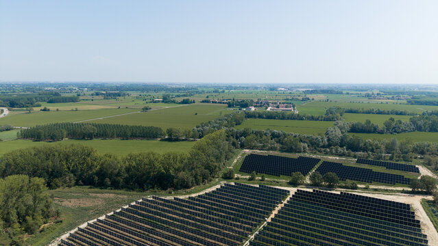 Aerial view of a large solar farm with rows of photovoltaic panels set in the green agricultural landscape of Cascina Maggiore, Lombardy, Italy.