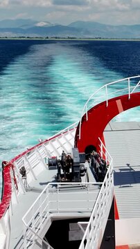 Panoramic vertical view from the ferry deck of the calm sea and mountainous coast, the trail of the ferry against the background of mountains and clouds.