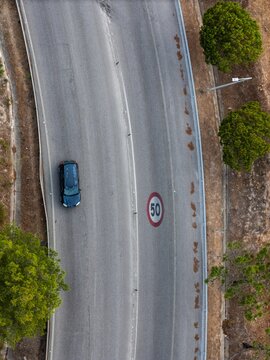 Aerial view of a car driving on a curved road with a painted 50 kmh speed limit sign, flanked by trees in Cascais, Lisbon, Portugal.