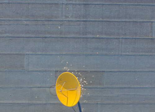 Aerial view of a bright yellow satellite dish mounted on a flat grey rooftop in Lisbon, Lisbon, Portugal.