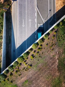 Aerial view of a taxi parked in a designated lane on a paved road with directional arrows and markings, adjacent to a concrete retaining wall and grassy area in Porto, Porto, Portugal.