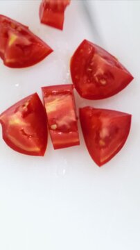 Fresh tomato cutting close up on white kitchen board. Chef hands in blue gloves mince red vegetable with big iron knife. Cooking, preparing ingredients in professional restaurant. Top down view