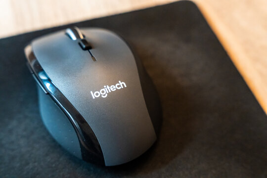 Warsaw, Poland - July 30, 2026: Logitech wireless computer mouse placed on black mousepad on wooden desk surface, side view showing brand logo and scroll wheel