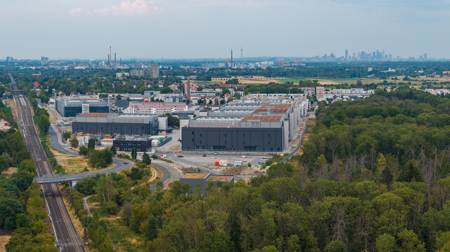 Aerial view of the NTT Global Data Centers Rechenzentrum Frankfurt 4 facility near railway tracks and forest with the Frankfurt skyline in Hattersheim am Main, Hessen, Germany.