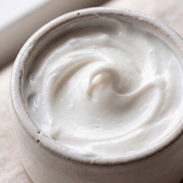 Macro close-up of swirled white face cream in a ceramic bowl with soft natural light