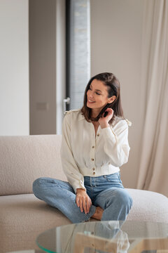 Full length of a cheerful smiling confident woman sitting on the couch in her modern home