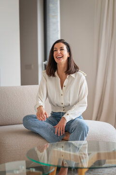 Full length of a cheerful smiling confident woman sitting on the couch in her modern home