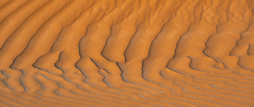 Aerial view of rippled orange sand dunes in a desert landscape with soft shadows.