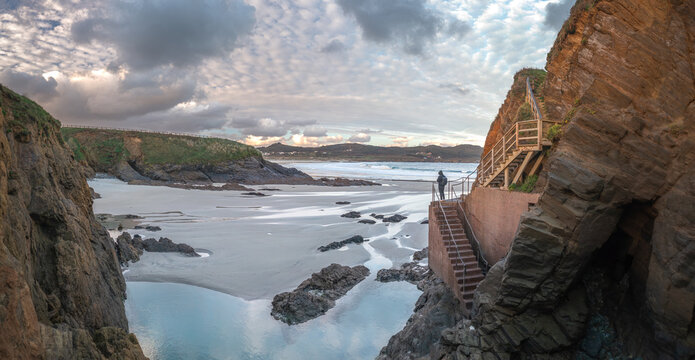 Aerial view of the rugged coastline near Ermita de Santa Comba with a person on a wooden staircase built into the cliffs and a sandy beach in Covas, La Coruna, Spain.