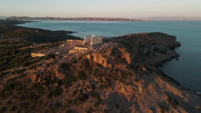 Sounion, Greece - 01 June 2026: Aerial view of the Temple of Poseidon on the rocky cliffs of Cape Sounion overlooking the Aegean Sea at sunset with crowds of people.