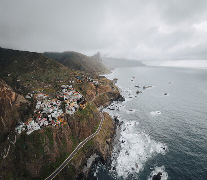 Aerial view of the coastal village of Almaciga with its winding road along steep cliffs and crashing waves under a cloudy sky in Santa Cruz de Tenerife, Canarias, Spain.
