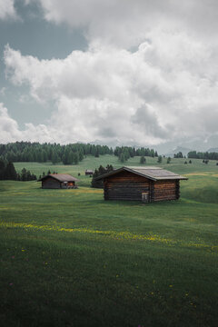 05 June 2024: View of traditional wooden cabins on a vast green meadow with rolling hills, a forest and mountains in the background under a cloudy sky.