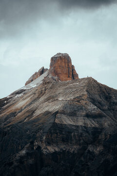 07 June 2024: View of a jagged mountain peak with a lone hiker standing on the edge of a steep ridge under a dark and grey cloudy sky.