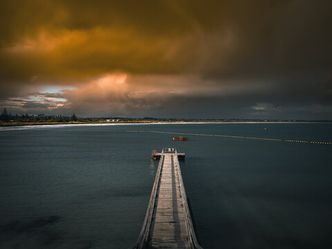 View of the wooden pier extending into the calm waters of Middleton Beach under a dramatic stormy sky in Middleton Beach, Western Australia, Australia.