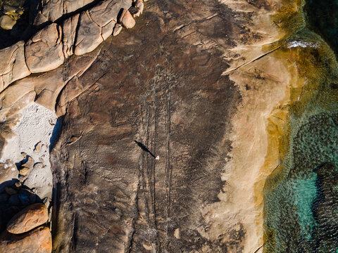 Aerial view of granite rock formations at Greens Pool with a person casting a long shadow on textured stone near turquoise ocean waters in Denmark, Western Australia, Australia.