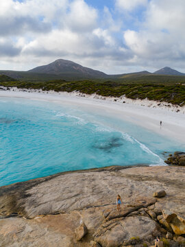 Aerial view of Hellfire Bay featuring turquoise waters, white sand, and rocky terrain with people on the beach and rocks in Cape Le Grand National Park, Western Australia, Australia.